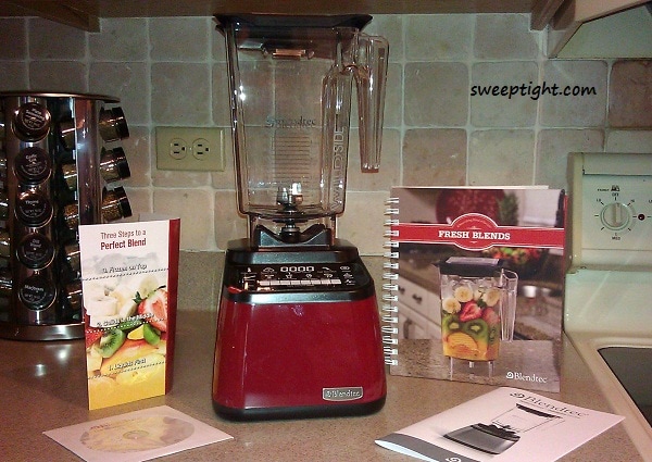 Blendtec blender on a counter with book and instructions it comes with. 