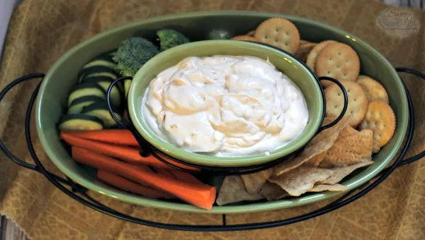 Creamy Chipotle Onion Dip in a dish surrounded by carrots, cucumbers, broccoli, chips, and crackers. 