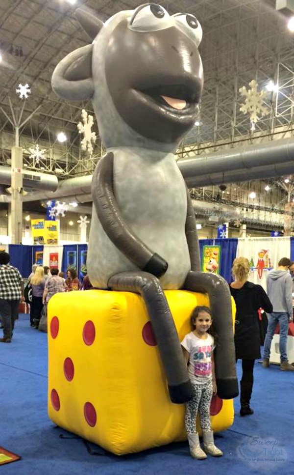 Mia standing in front of a huge sheep sitting on cheese at the Chicago Toy and Game Fair. 