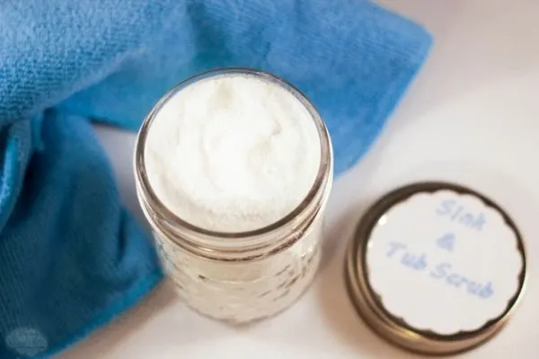 An open jar of sink cleaner next to a blue towel and lid. 