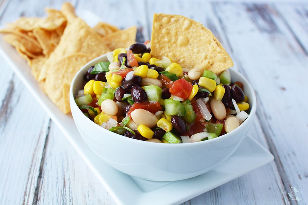A bowl of bean salad with tortilla chips. 