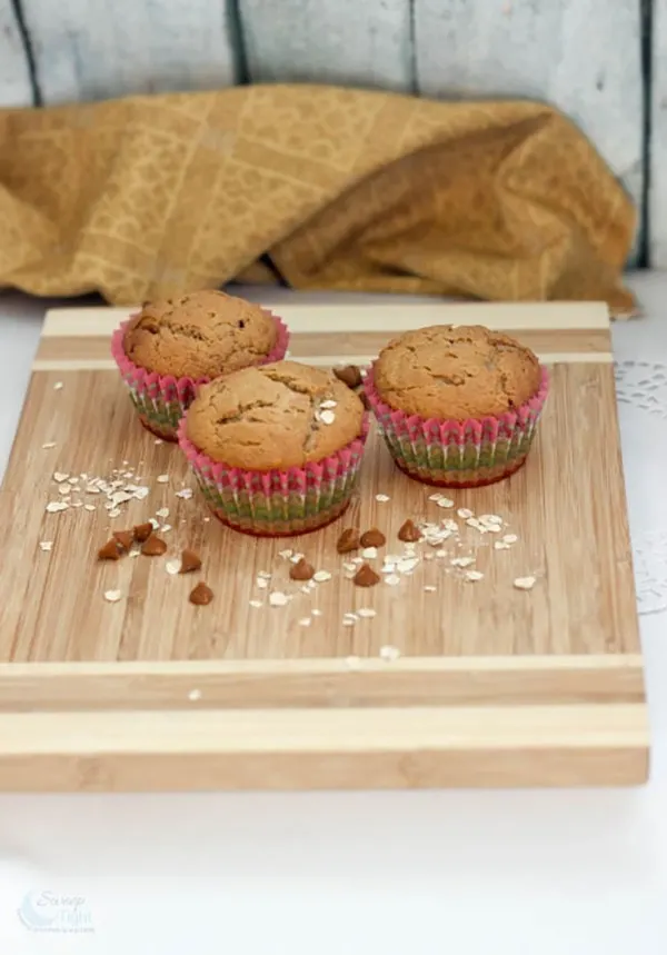 Three peanut butter muffins with chips sitting on a board. 