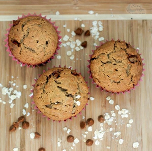 Three muffins on a cutting board with chips and oats. 