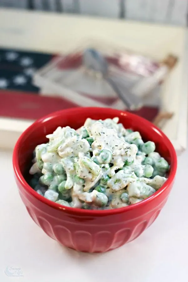 Pea salad in a red bowl with flag decor on the table. 