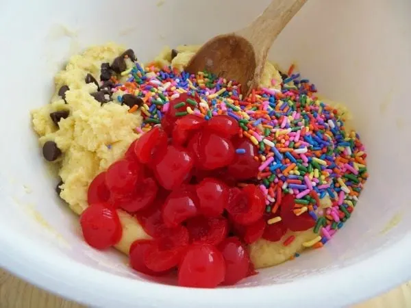 Cherries, sprinkles, chocolate chips, and cake mix in a bowl. 