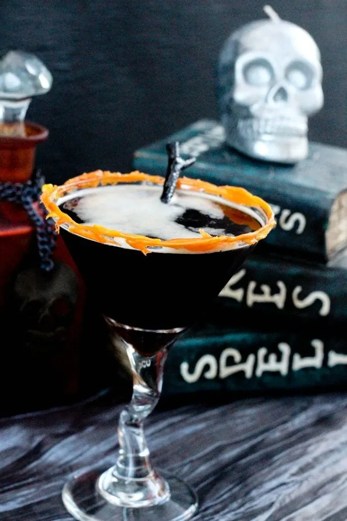 Coffee drink in a martini glass with skulls and spooky books on the table. 