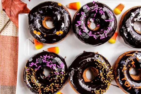 Gingerbread donuts with Halloween sprinkles on a white serving platter with fall decor on the table.