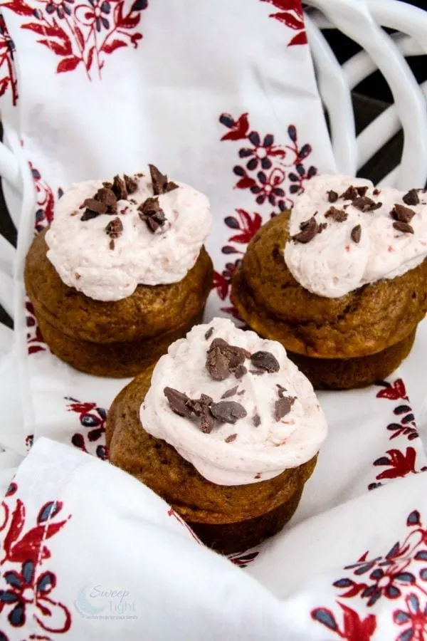 Pumpkin muffins with cranberry frosting and chocolate shavings on a napkin. 