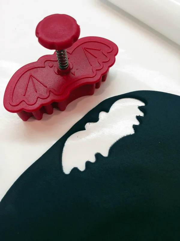 Using a cookie cutter to create bat shapes out of black fondant. 