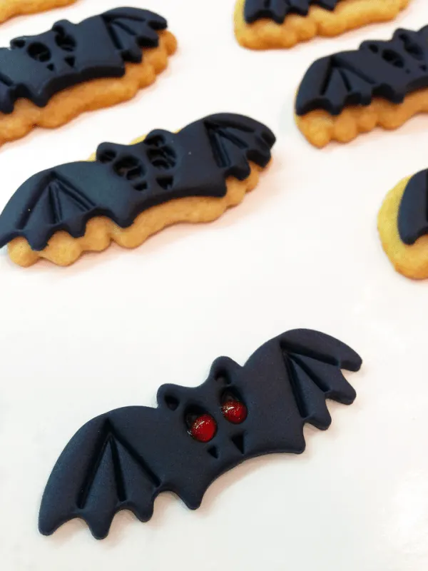 Black fondant in the shape of bats on top of bat sugar cookies. 