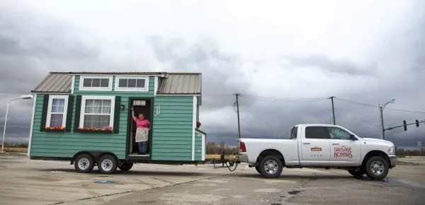 A truck pulling a tiny home with a women waving in it. 