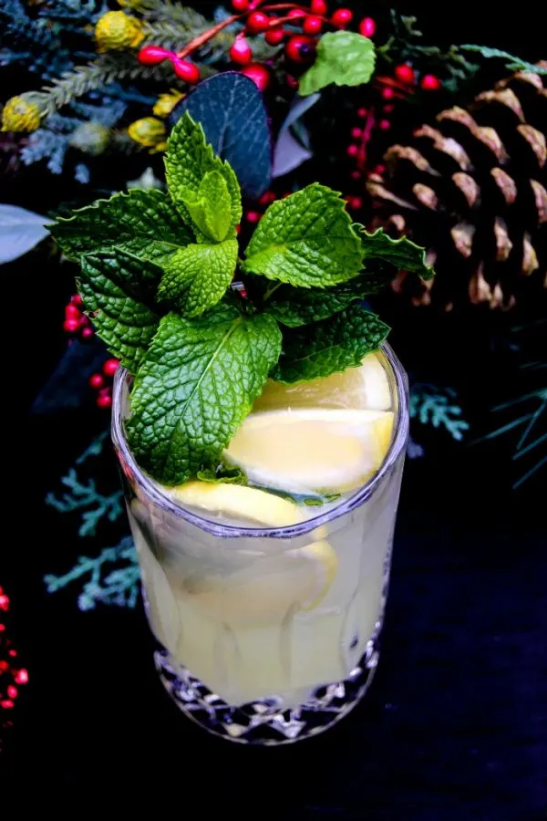 Glass of lemonade with lemons and mint springs next to Christmas decor. 