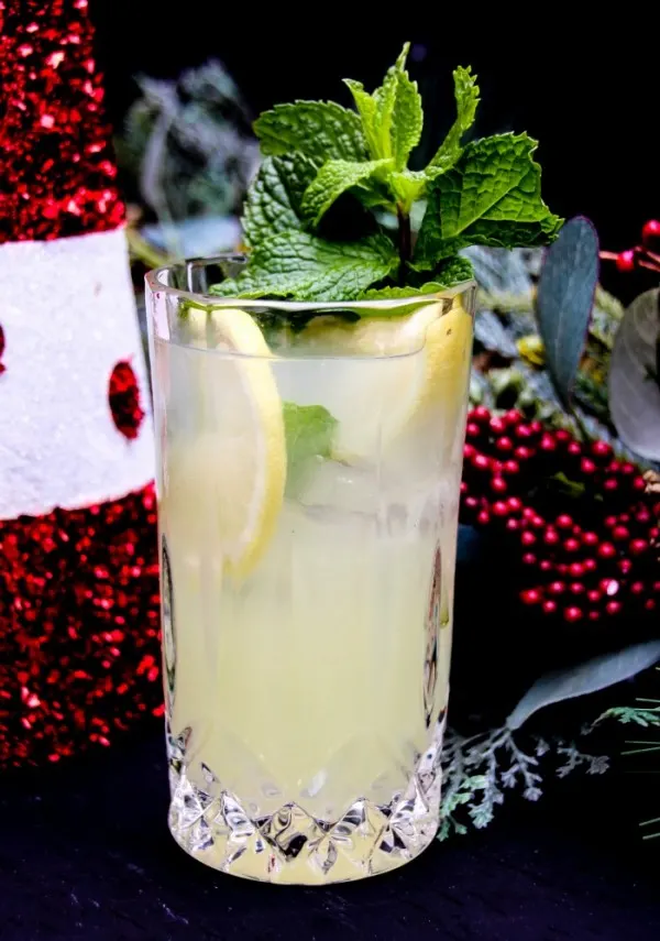 Lemon drink with mint and lemon slices next to holiday decorations. 