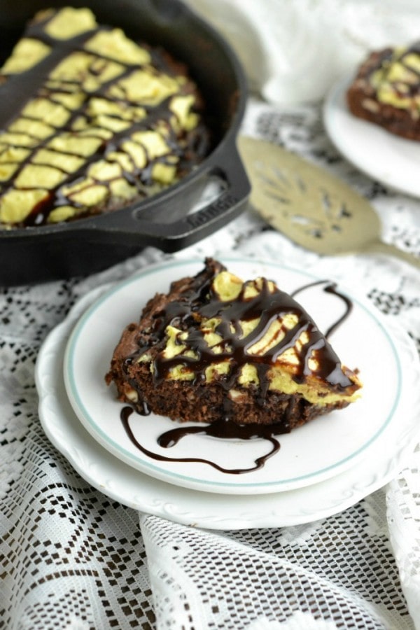 A chocolate chip cookie cake in a skillet on a plate topped with chocolate syrup. 