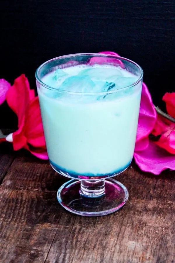 Bright blue drink in a glass with pink flowers around it