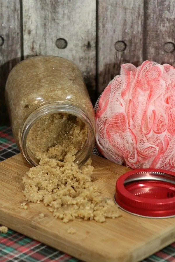 Gingerbread sugar scrub dumped out of a mason jar next to a pink loofah. 