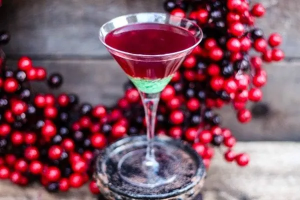 Green candy cane peppermint martini next to holiday berries. 