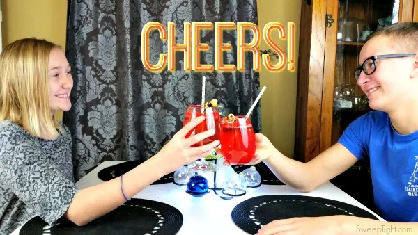 Two kids holding glasses to cheers a sparkly red kid-friendly drink.