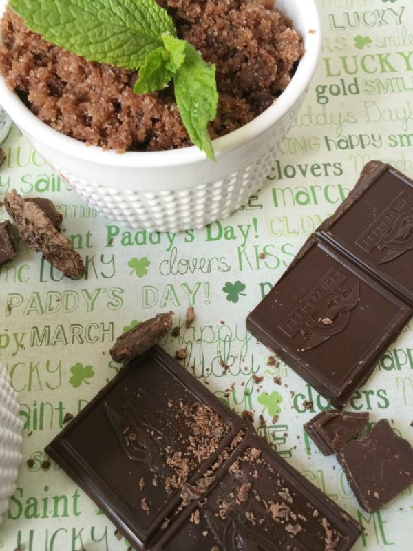 Chocolate sugar scrub with mint leaves in it next to chunks of chocolate. 