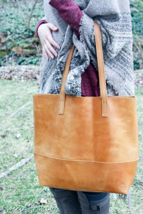 Tan leather purse being held by a woman in a scarf. 