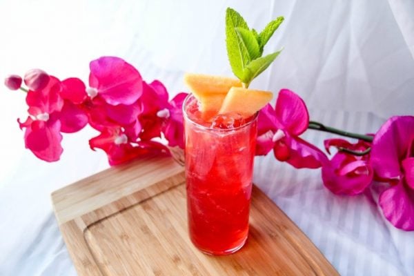A red drink on a board next to flowers. 
