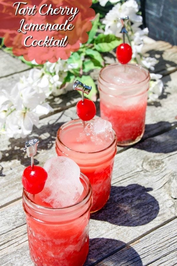 Jars of tart cherry juice lemonade cocktails sitting next to flowers. 
