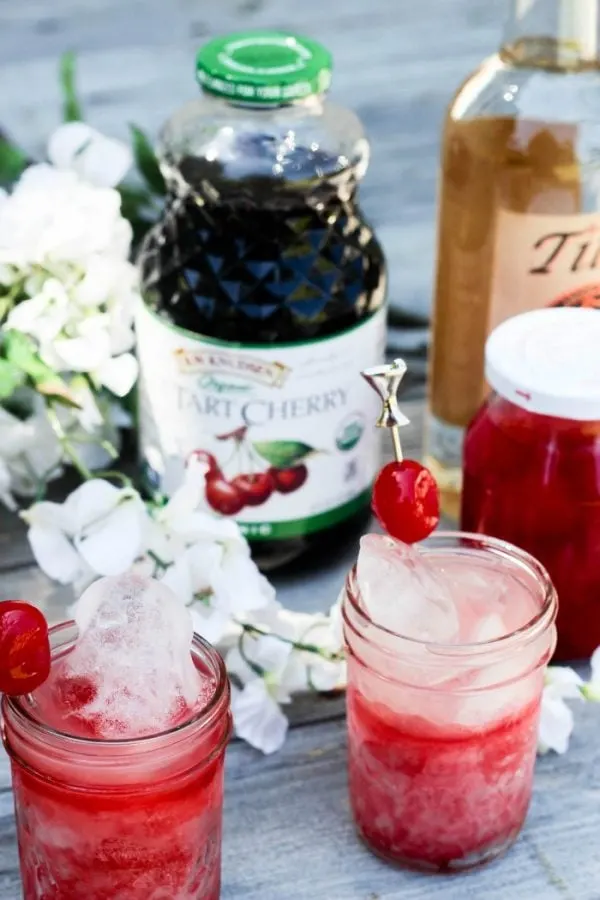 Dark cherry juice, cherries, Tito's, and red drinks on a table. 