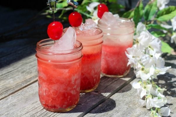 Three jars of red lemonade next to flowers. 