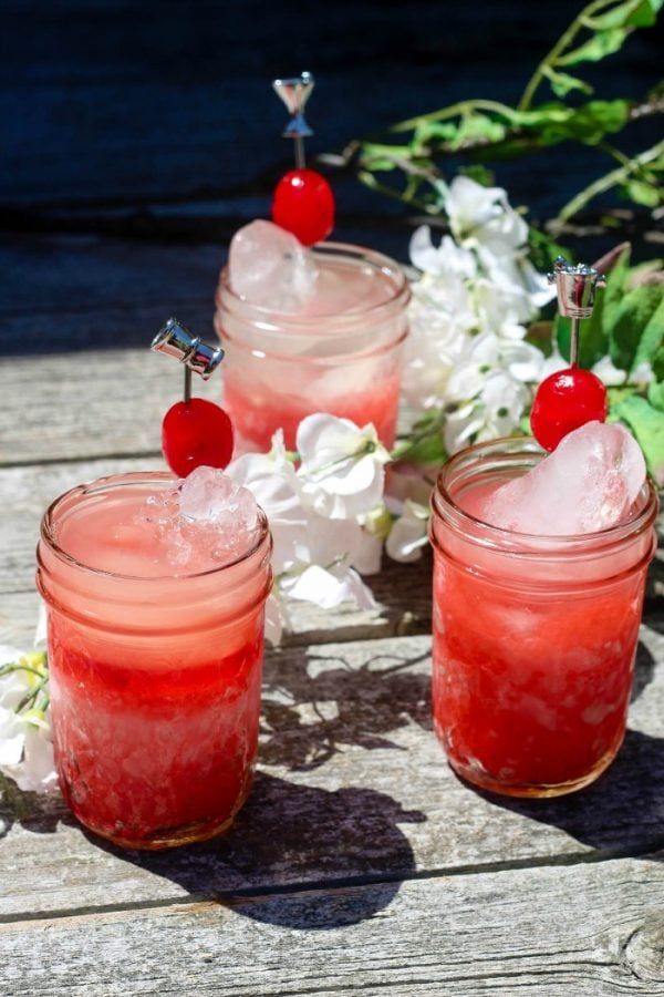 Three jars of cherry lemonade with ice and cherries on picks. 