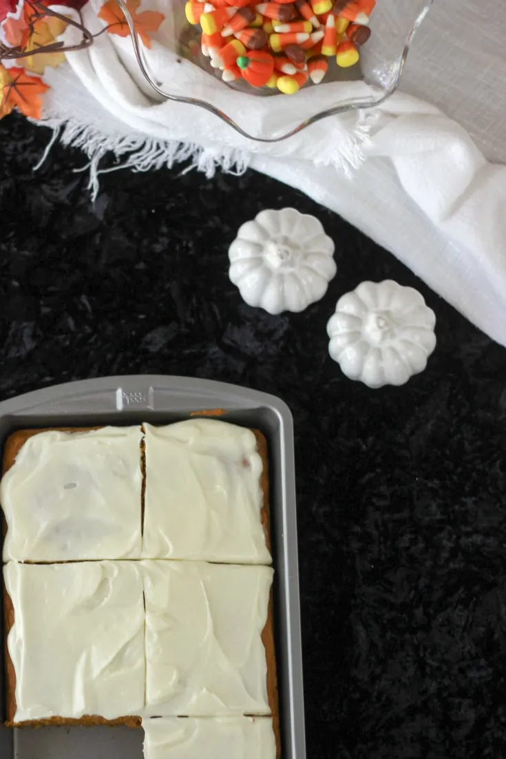 Pumpkin squares in a baking pan on a table with pumpkins and fall decor. 