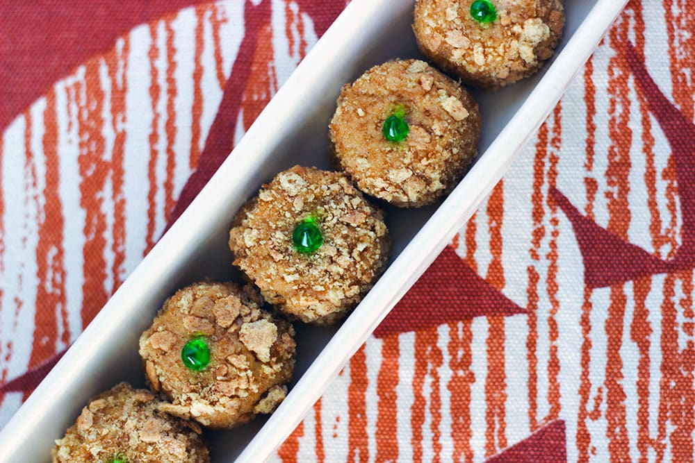 Pumpkin oreo balls with a green dot on top lined up in a narrow tray on a table. 