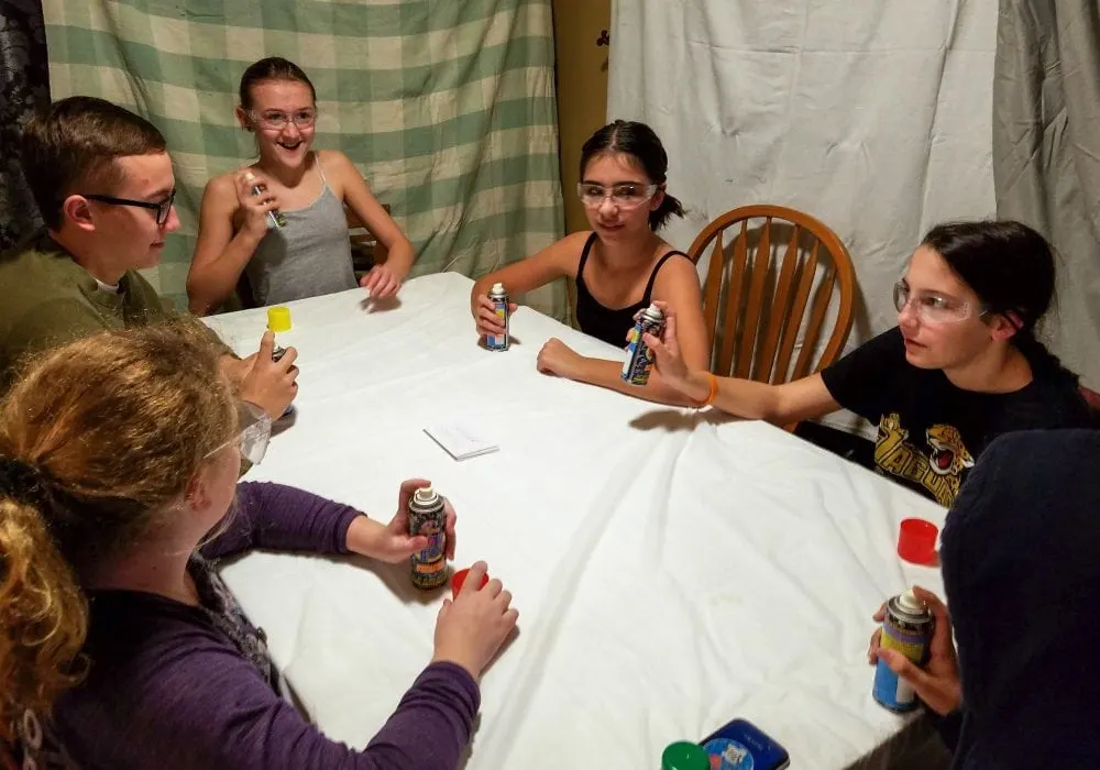 Kids wearing safety glasses holding cans of Krazy string sitting around a table. 