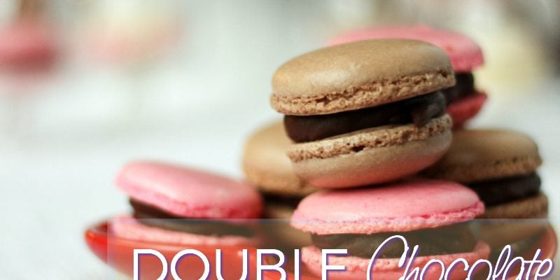 Double chocolate macarons on top of pink macarons on a plate. 