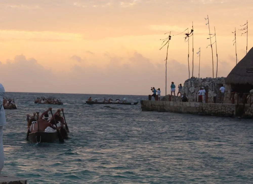 The Sacred Mayan Journey canoes in the water with onlookers standing by. 