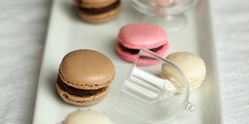 Mini macarons in brown, cream, and pink, on mini cake stands.