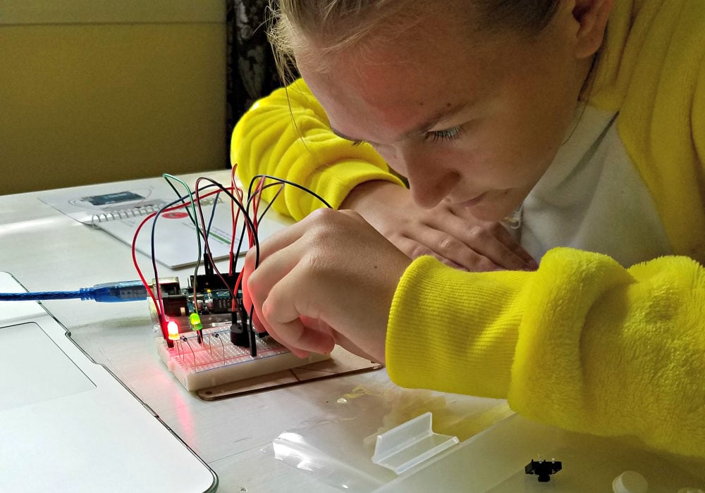 Girl hooking a wire into a little circuit board. 