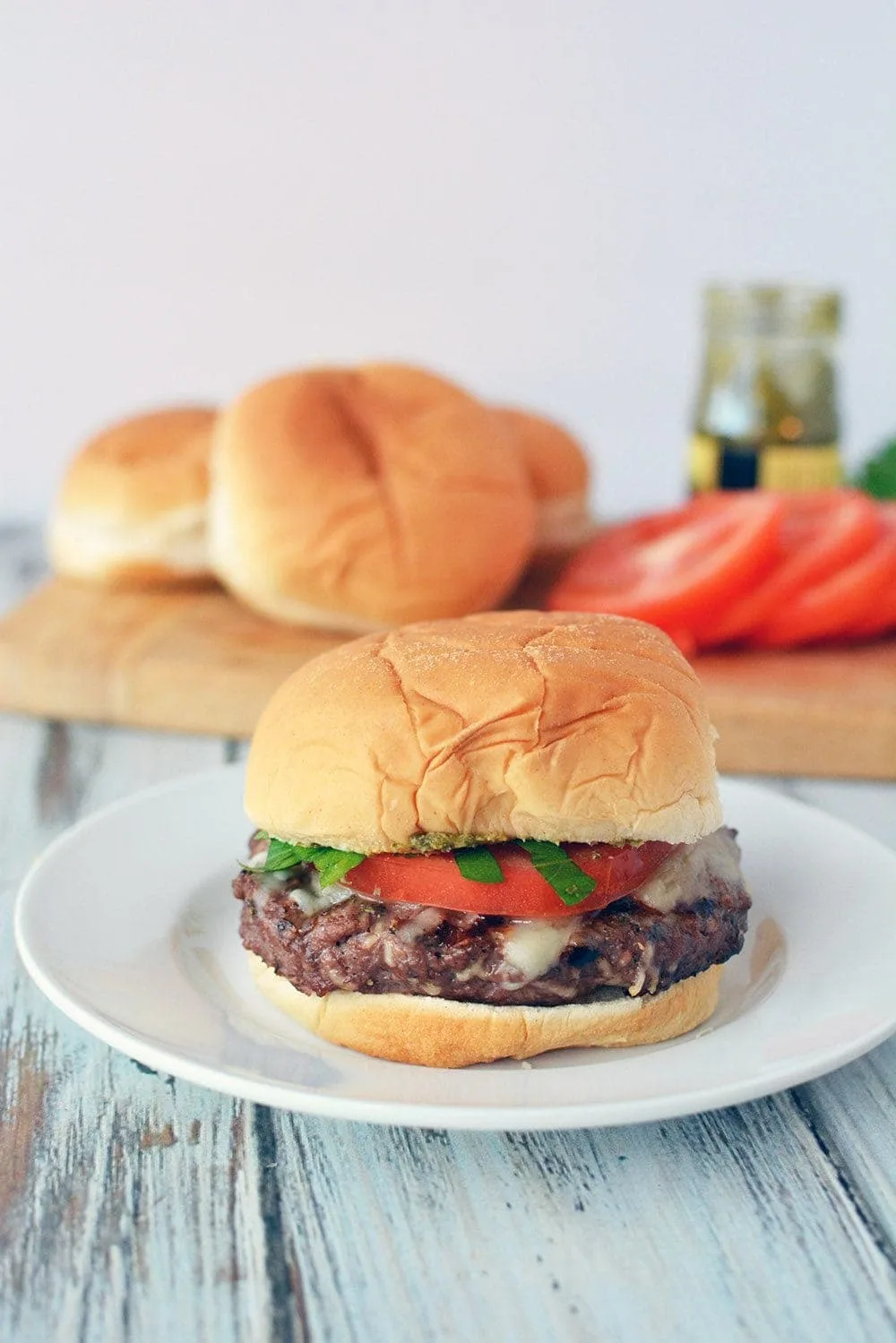 Burger with a bun on a plate topped with tomato and lettuce. 