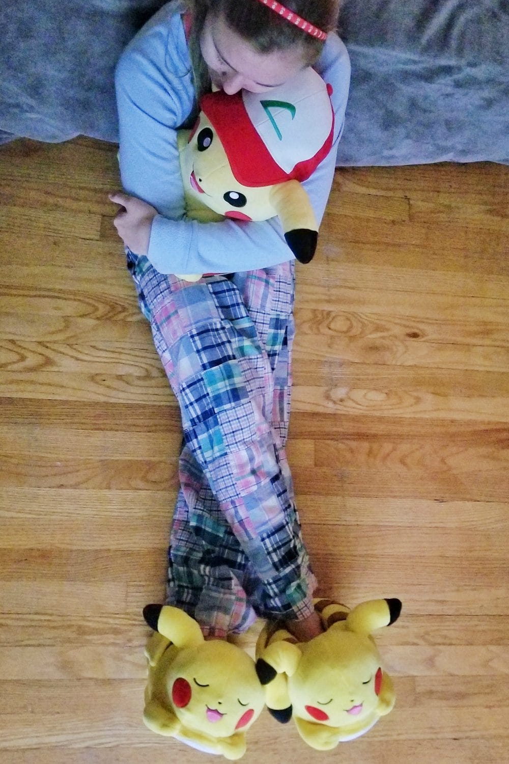 Chesney hugging a plush Pikachu while wearing Pokemon slippers. 