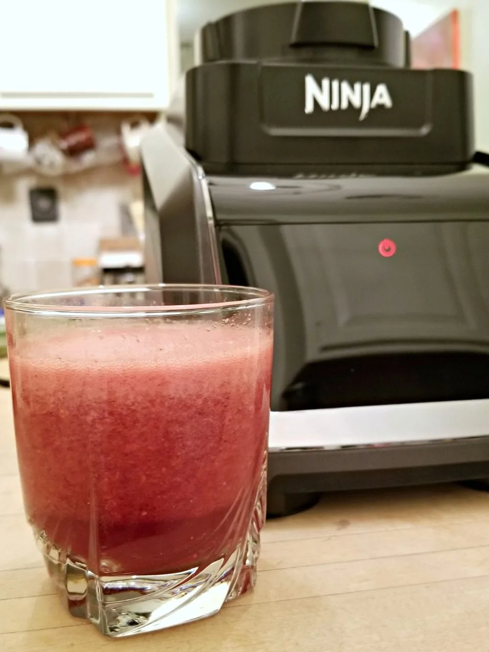 Glass of cherry drink next to a blender. 