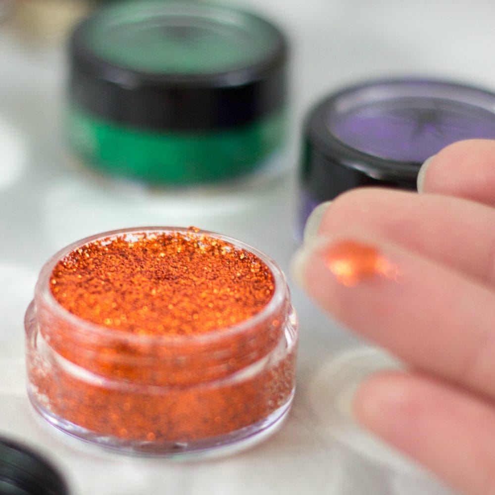 Orange glitter eyeshadow and a dab on a finger. 