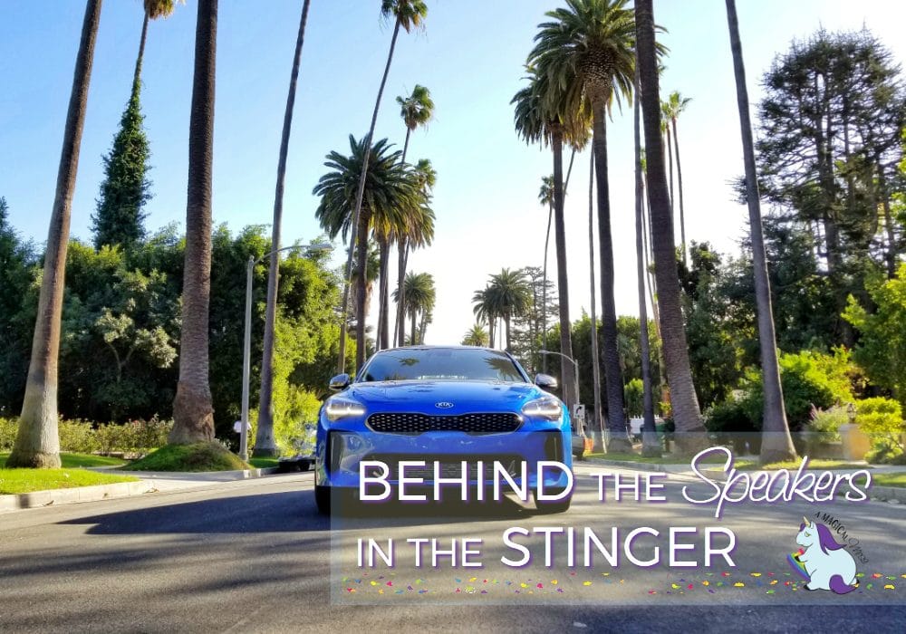 Blue Kia Stinger driving on a street lined with palm trees. 