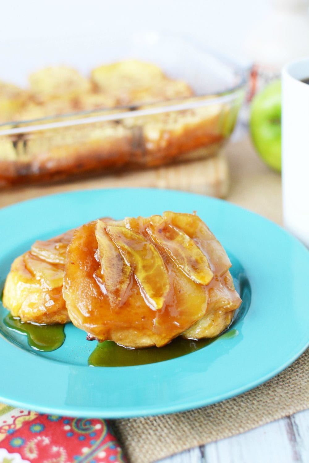 French Toast topped with apples on a plate with the rest in the background in a dish. 