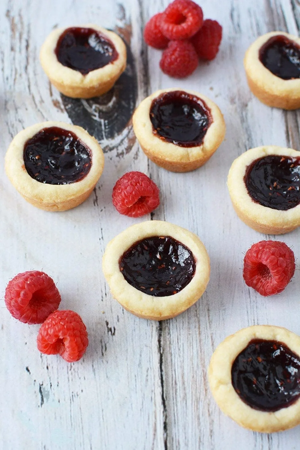 Mini raspberry tarts on a table with fresh raspberries. 