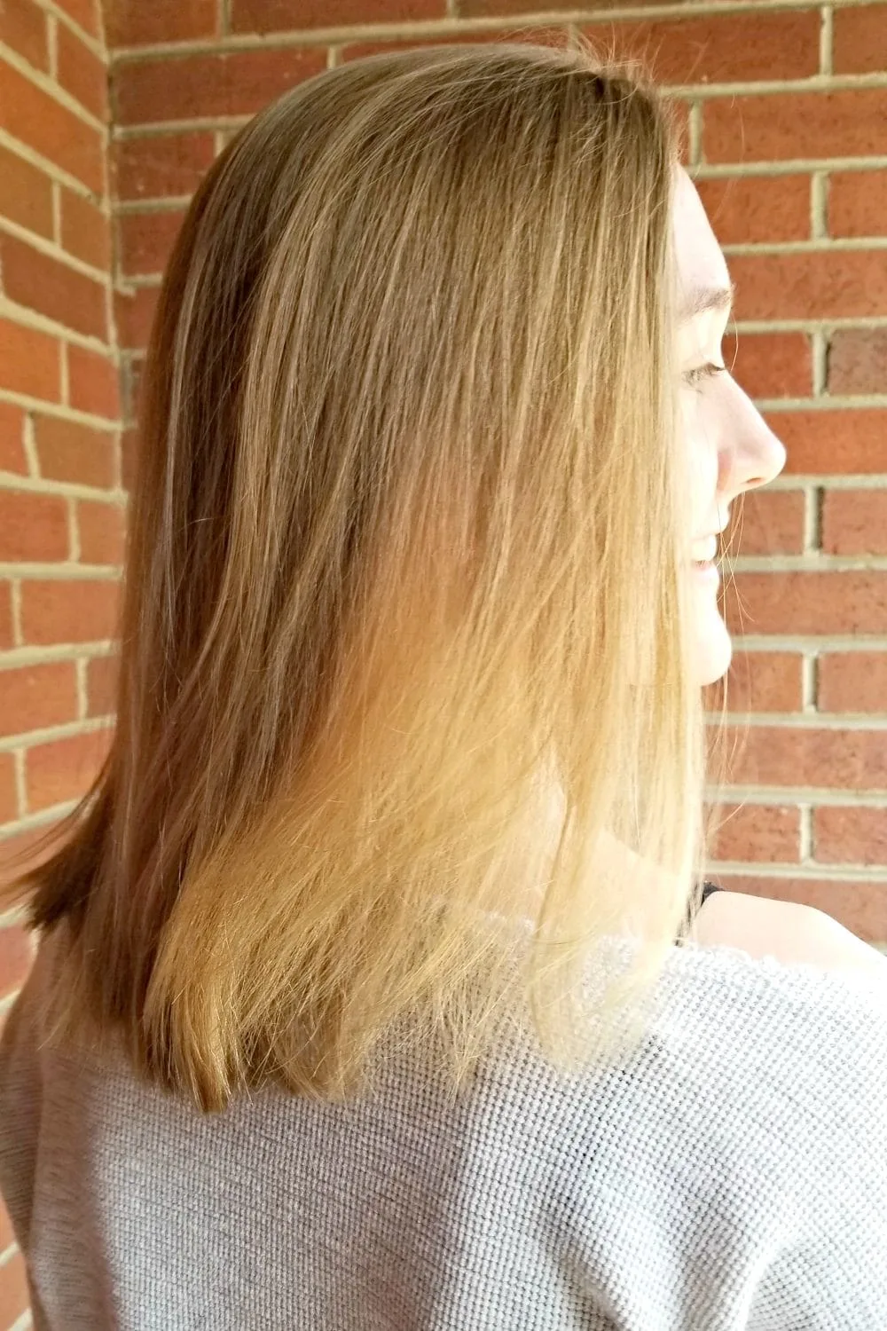 Girl with blondish hair standing by a brick wall. 