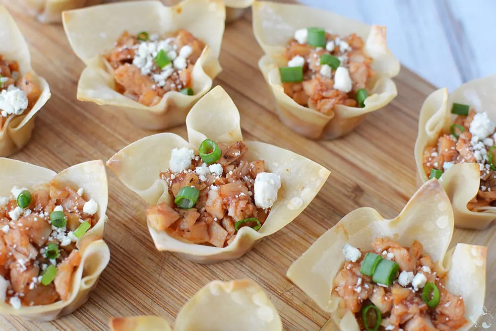 Shredded chicken in wonton cups on a board.