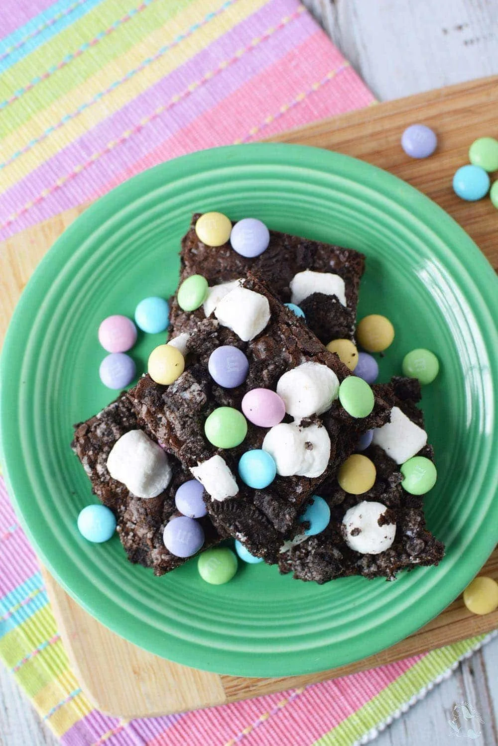Brownies with marshmallows and candy topping on a green plate. 