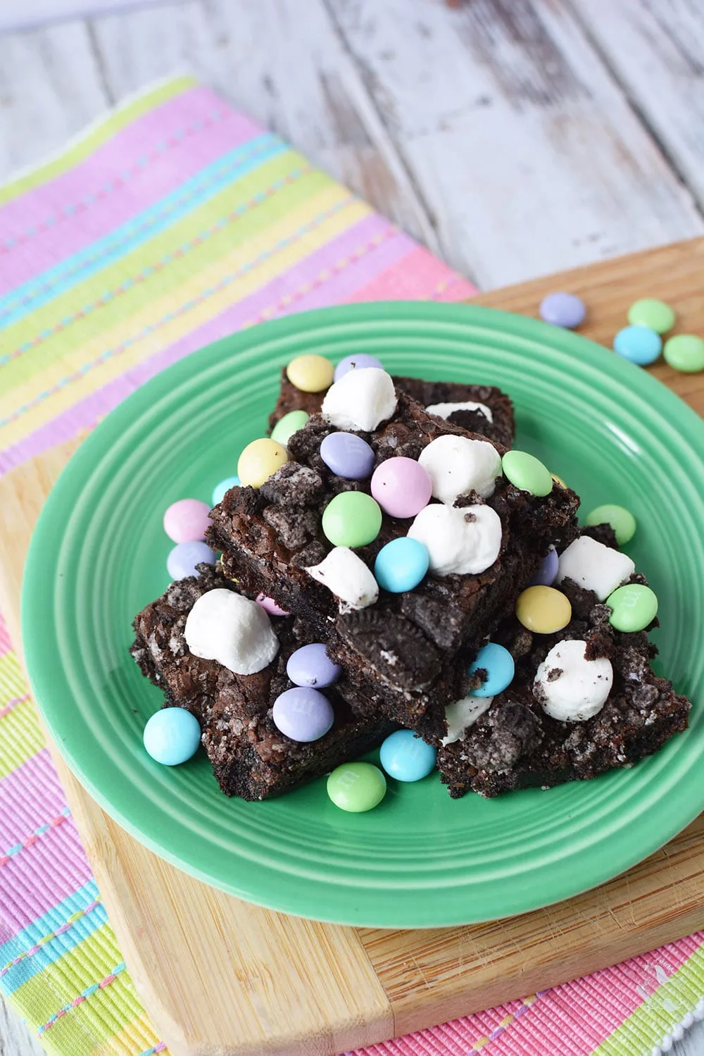 Brownies with marshmallows and M&Ms candy on a green plate. 