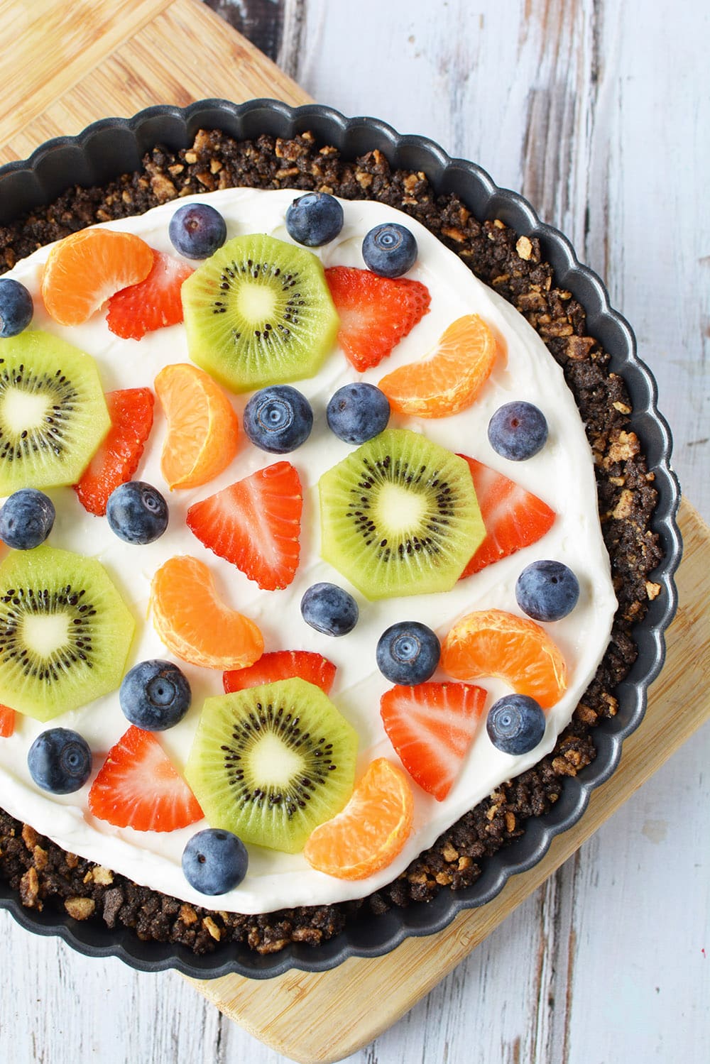 A tart pan with sugar cone crust topped with cream cheese frosting and fresh fruit. 