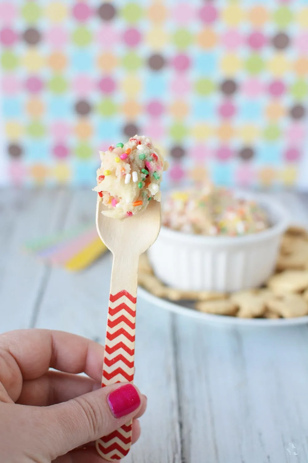 Rainbow cookie dough with sprinkles on a wooden spoon. 