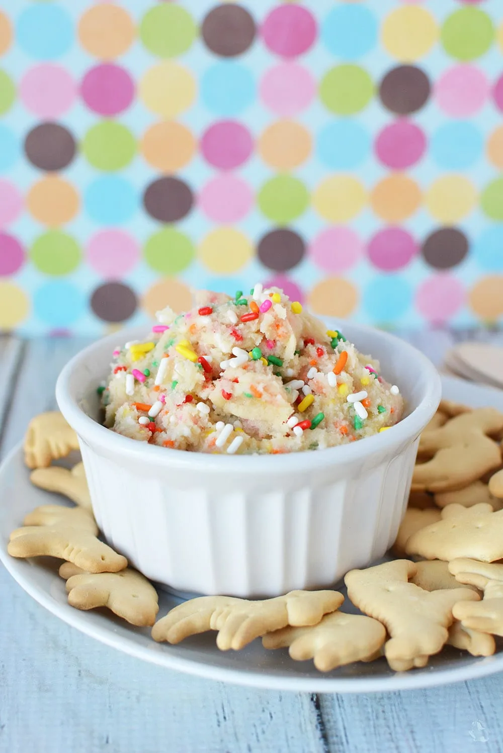 Ramekin filled with cookie dough topped with sprinkles surrounded by animal crackers on a plate. 